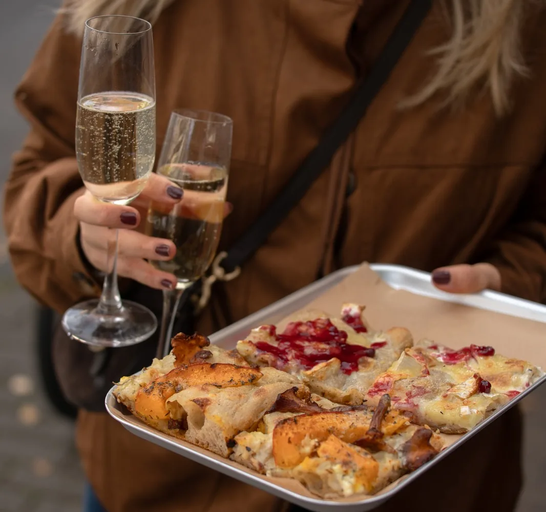 Blech mit zwei Stücken und zwei Gläsern Sekt in der Hand