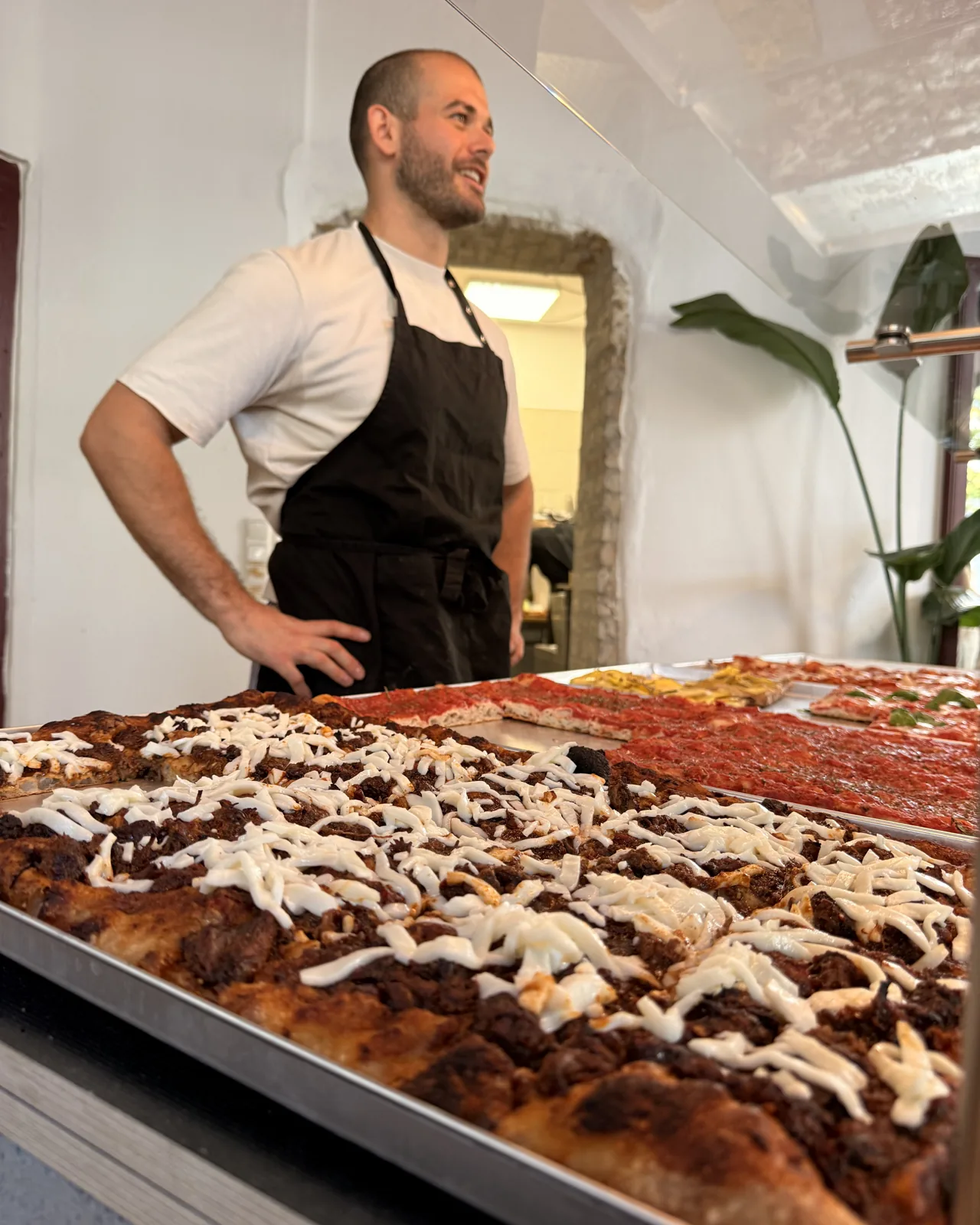 Pizzaiolo hinter der Theke, die Bleche vor ihm