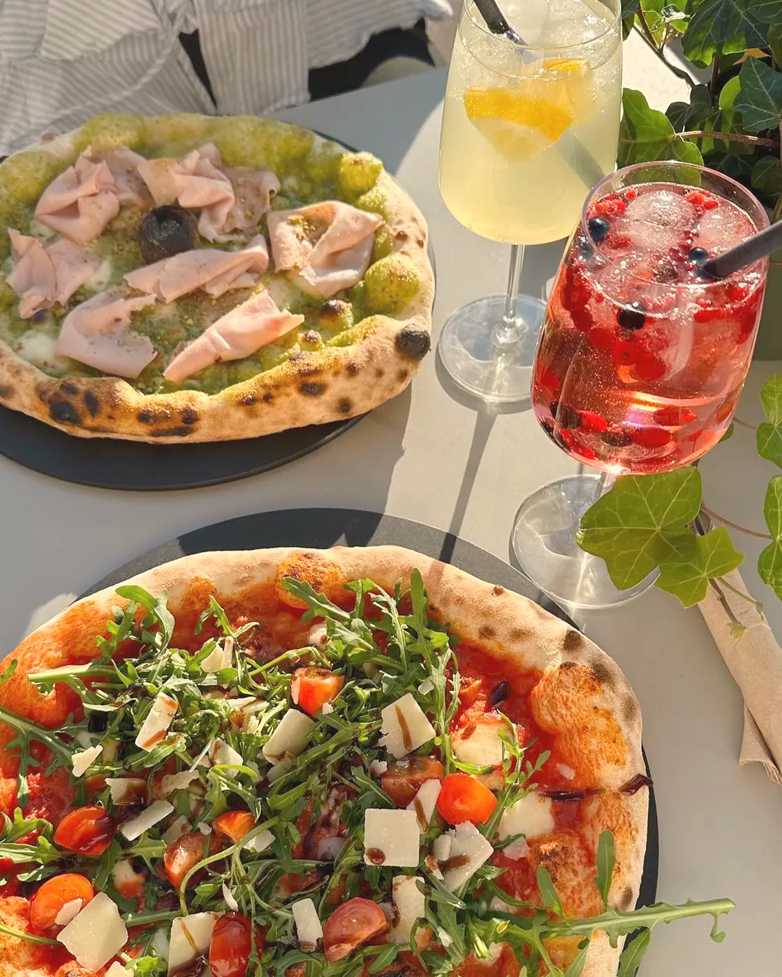 Pizza mit Schinken, Pistazie und Mozzarella, daneben Getränke